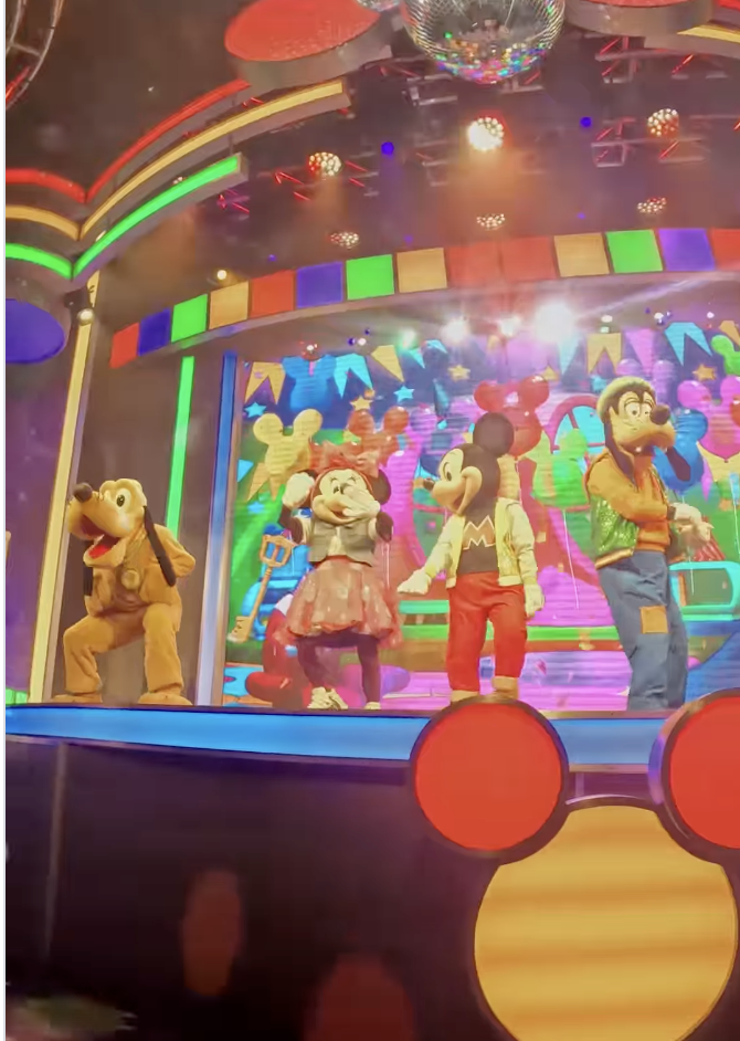 Pluto, Minnie Mouse, Mickey Mouse and Goofy perform on a colorful stage with bright lights, balloons 