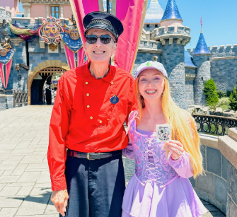 Eldery man Cast Member & young blonde woman posting front of Disneyland Castle