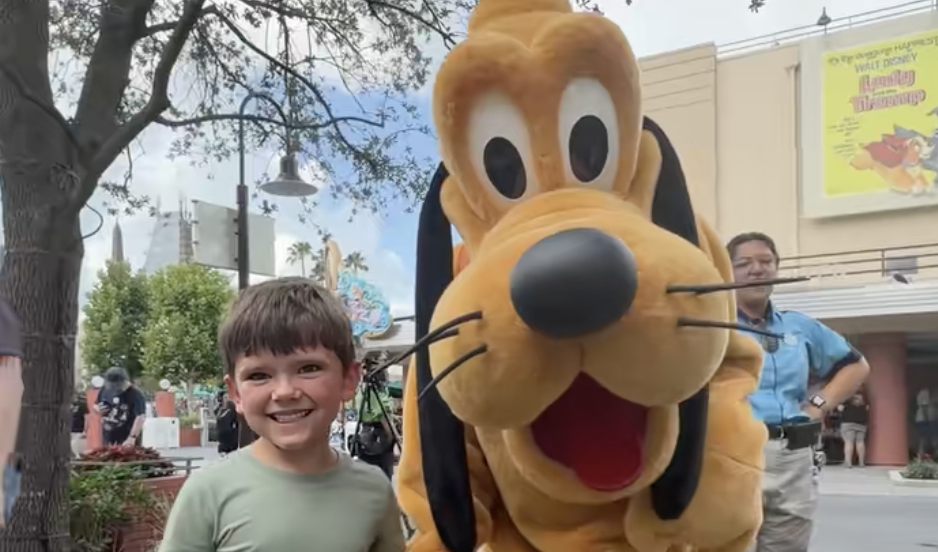 A child poses beside Pluto on a street