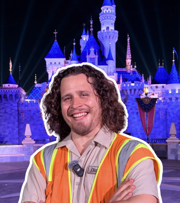 A Disneyland Resort Cast Member wearing a reflective safety vest stands with folded arms in front of Sleeping Beauty Castle illuminated at night.