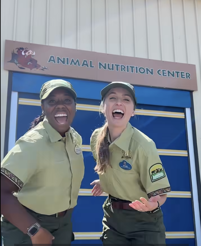 Two Walt Disney World Ambassadors stand in front of the Animal Nutrition Center sign during Animal Care Appreciation Week.