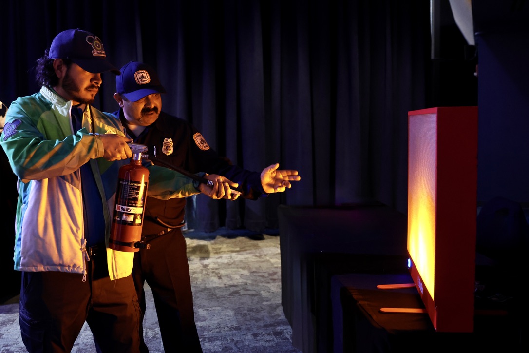 Firefighter Jesse Velarde teaching Disney PhotoPass cast member Juan Carlos Estuvier how to extinguish a fire using the PASS method on the BullEx Bullseye Digital Fire Extinguisher Training System. 