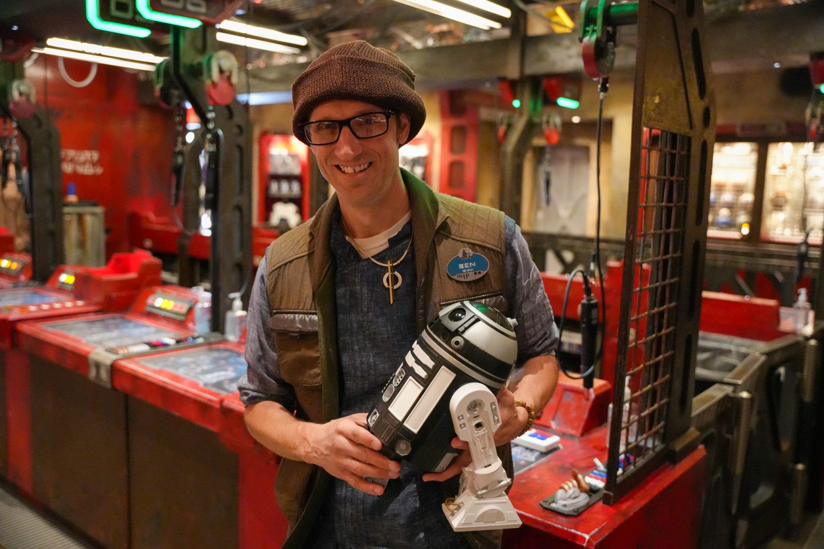 Ben, a retail cast member in Star Wars Galaxy’s Edge, smiles while holding a droid in Droid Depot. 